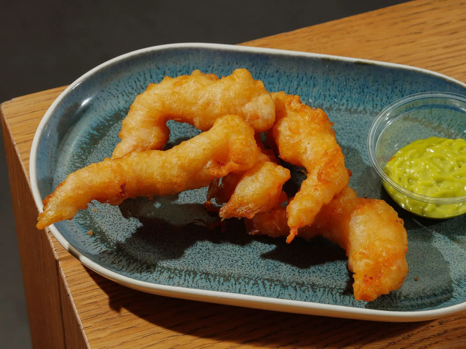 A delicious plate of crispy shrimp tempura served with green dipping sauce on a ceramic plate.